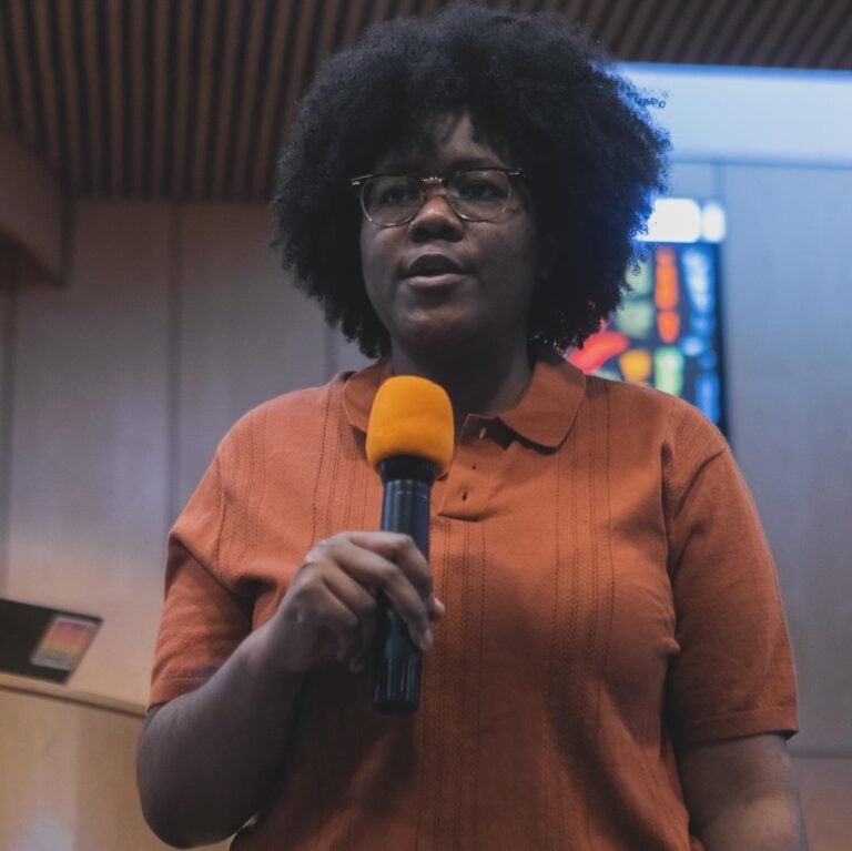 Ace Sutherland, a Black, non-binary person, speaks into a microphone.